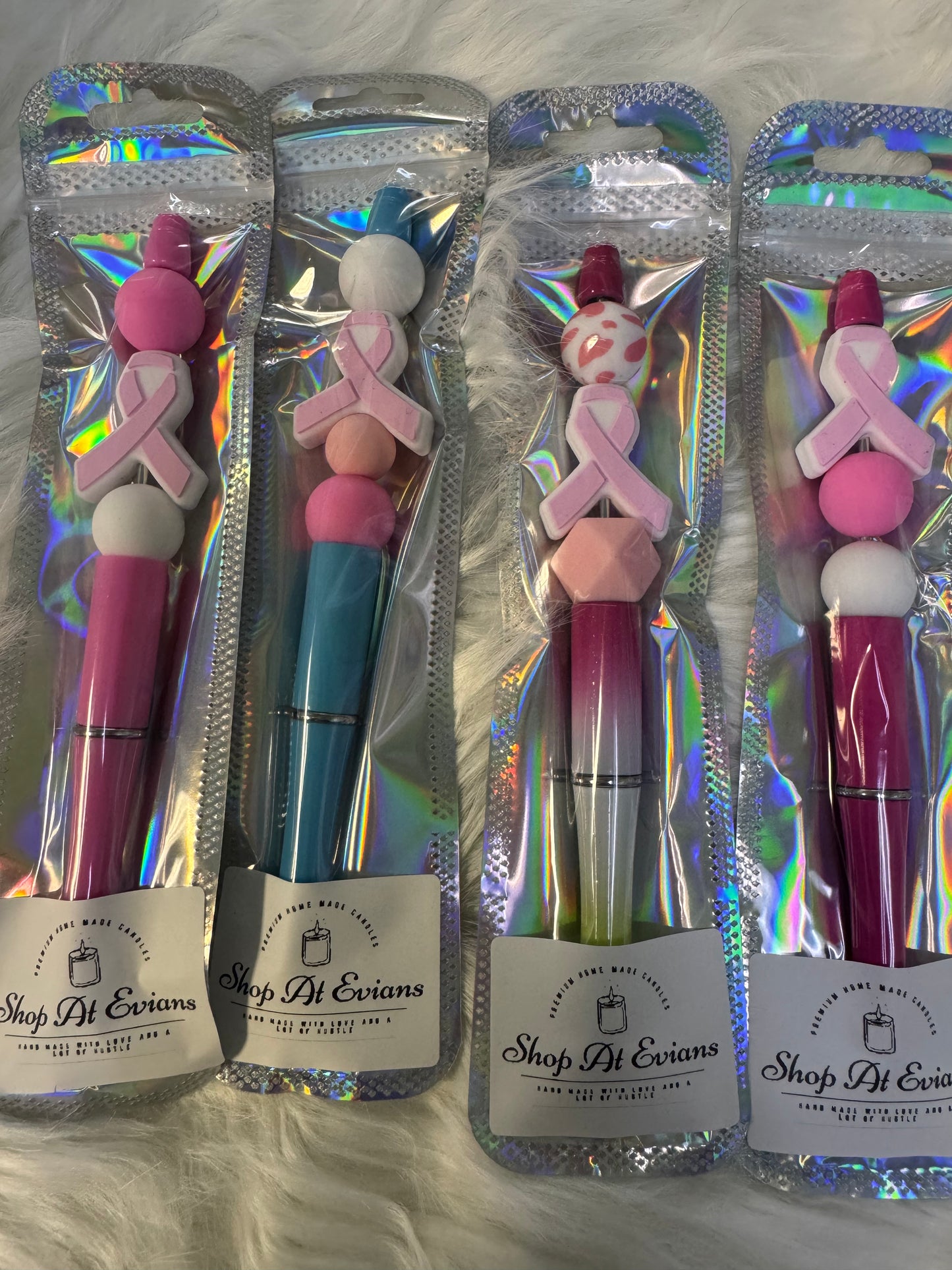 Four pens with colorful tops and breast cancer awareness ribbons in their packaging on a textured surface.