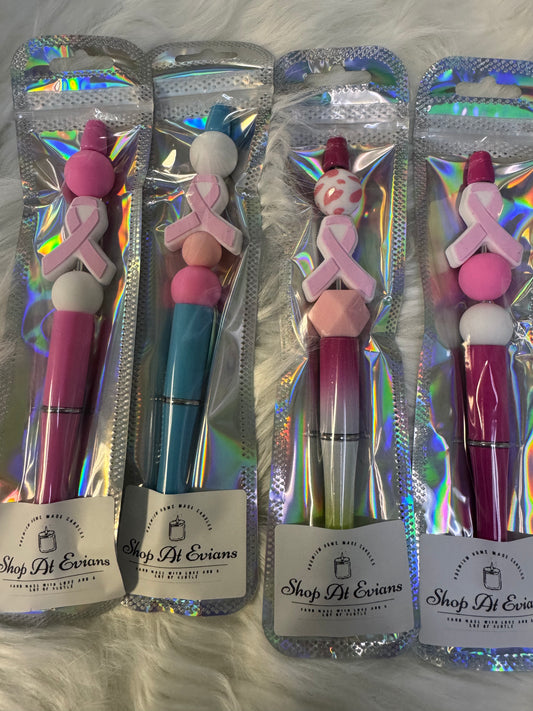 Four pens with colorful tops and breast cancer awareness ribbons in their packaging on a textured surface.